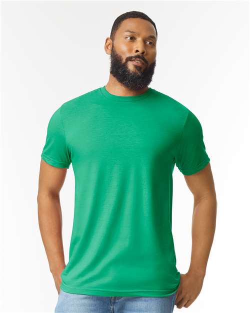 A bearded man stands against a plain white background with his hands by his sides, wearing blue jeans and a bright green Gildan Softstyle 64000CVC t-shirt from Gildan.