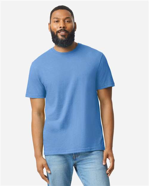 A bearded man with short hair wears a Gildan Softstyle 64000CVC t-shirt and light blue jeans, standing against a plain white background.
