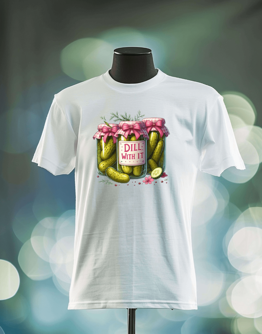 The Dill With It t-shirt by DB Custom Creations features a DTF print of a pickle jar with a pink bow and “DILL WITH IT” label, displayed on a mannequin against a softly glowing, colorful background.