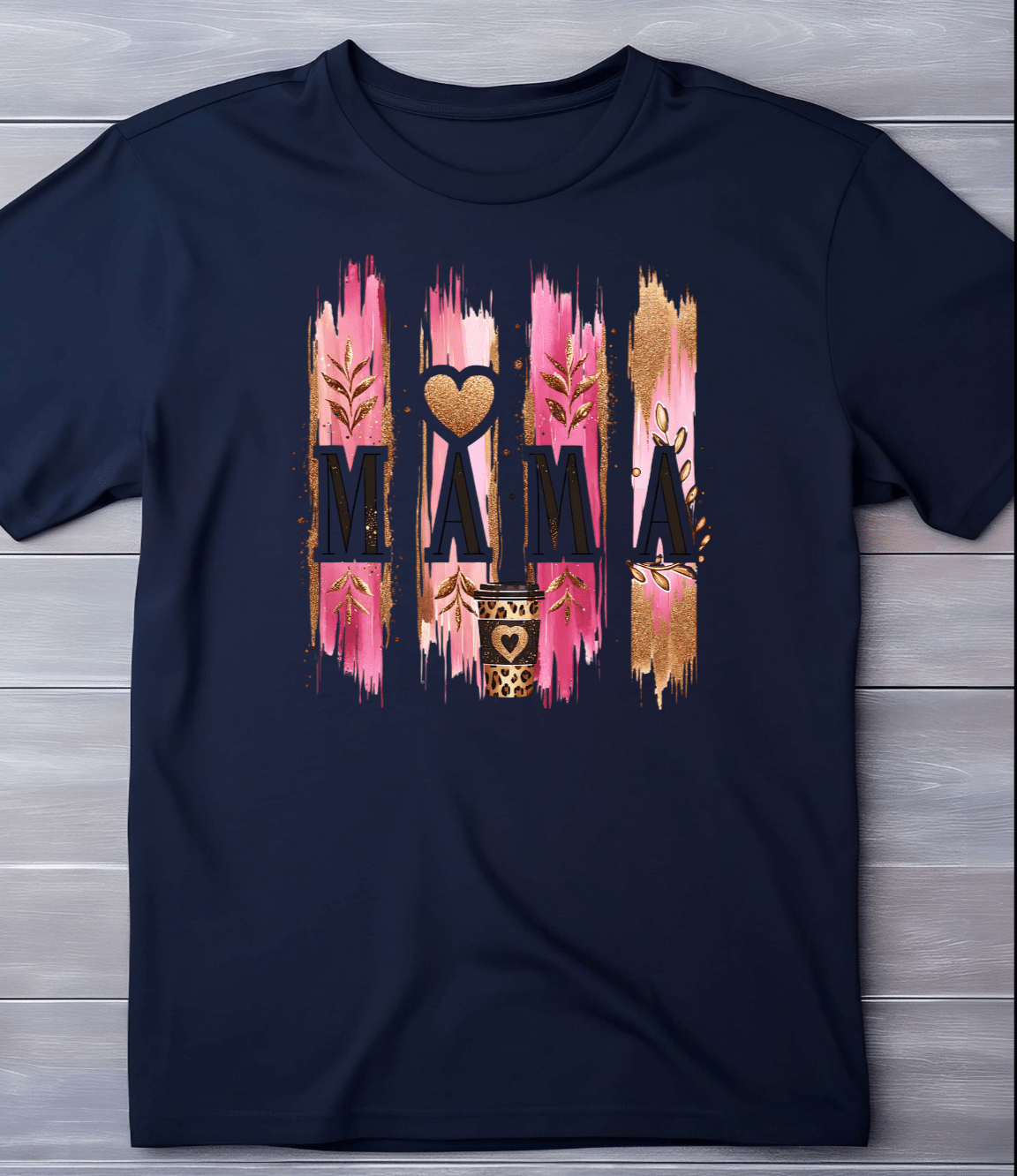 The Mama Coffee T-shirt by DB Custom Creations displays MAMA with a heart as the second A, set on a pink and gold brushstroke background with leaf and heart accents, printed using an 11 DTF transfer for vibrant, lasting color.