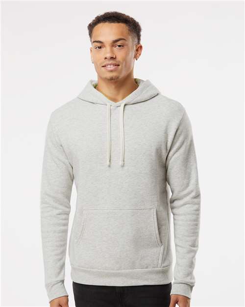 A young man is smiling while wearing the Next Level 9302 light gray cotton-polyester fleece hoodie with a front pocket, standing against a plain white background.