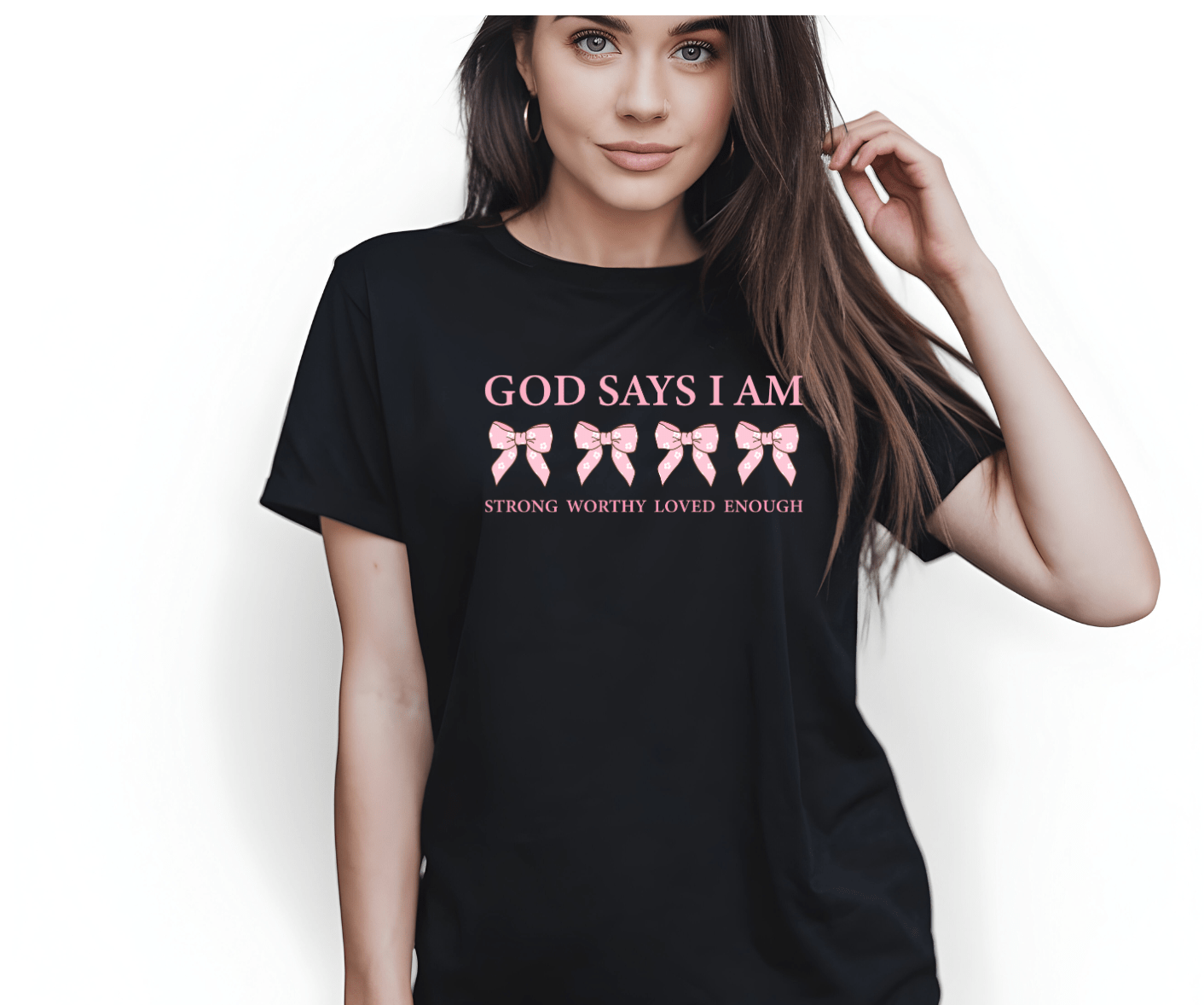 A woman with long hair wears a black God says I am t-shirt by DB Custom Creations, featuring pink bows and the words STRONG, WORTHY, LOVED, ENOUGH in pink on a high-quality 11-inch DTF transfer. The background is white.
