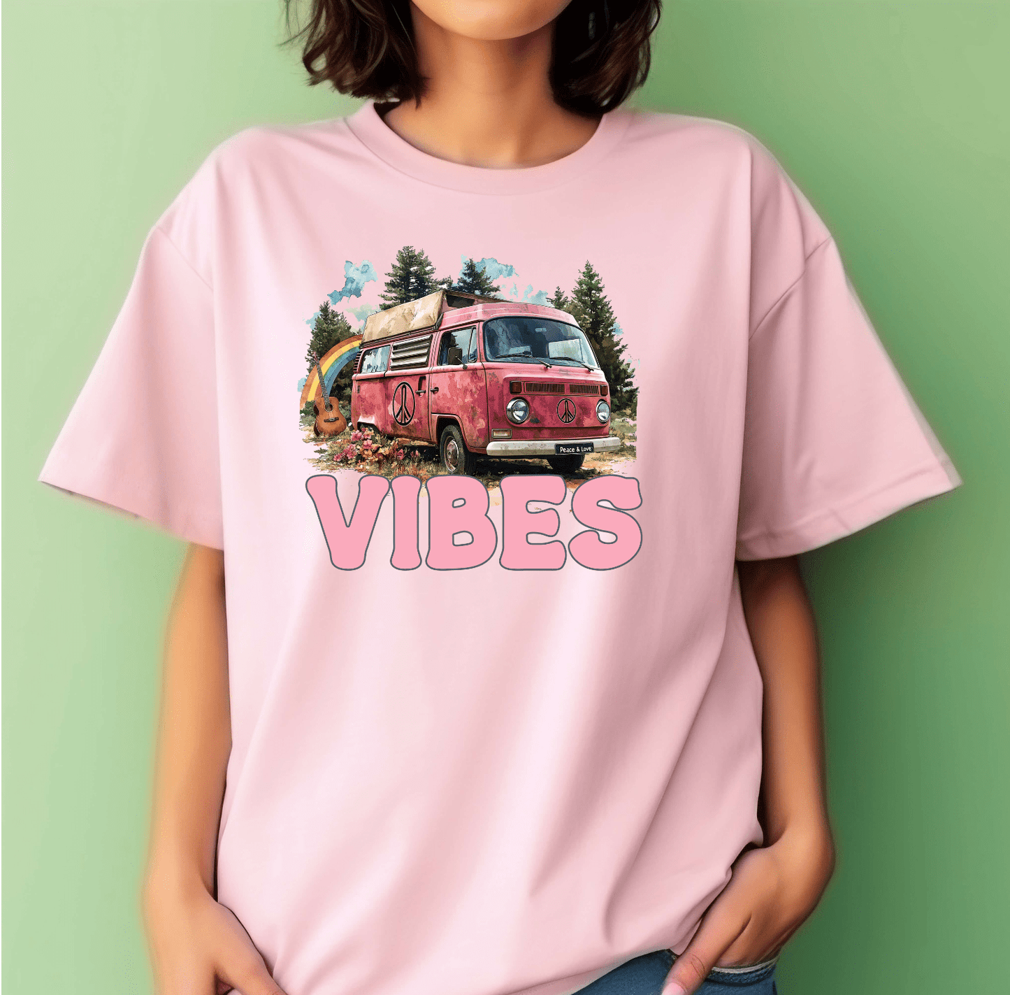 A person wears a DB Custom Creations Hippie Vibes pink t-shirt with an illustrated pink vintage van, peace signs, trees in the background, and VIBES in bold, made using an 11-inch DTF heat transfer.
