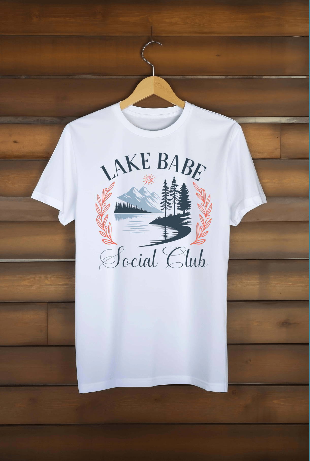 The Lake Babe Social Club white t-shirt by DB Custom Creations features “Lake Babe Social Club” text and a mountain, trees, lake, sun, and red leaf design on the front with vibrant 11 DTF printing.