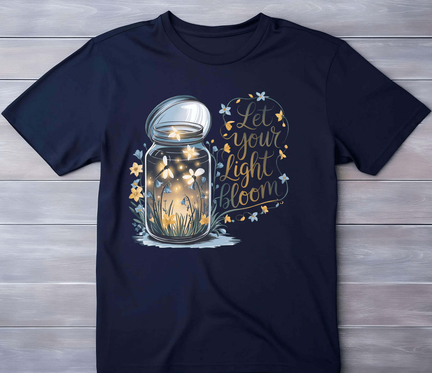 The “Let your light Bloom” navy tee by DB Custom Creations features an 11 DTF print of a glowing firefly and flower jar, with “Let your light bloom” in yellow script, surrounded by stars and flowers.