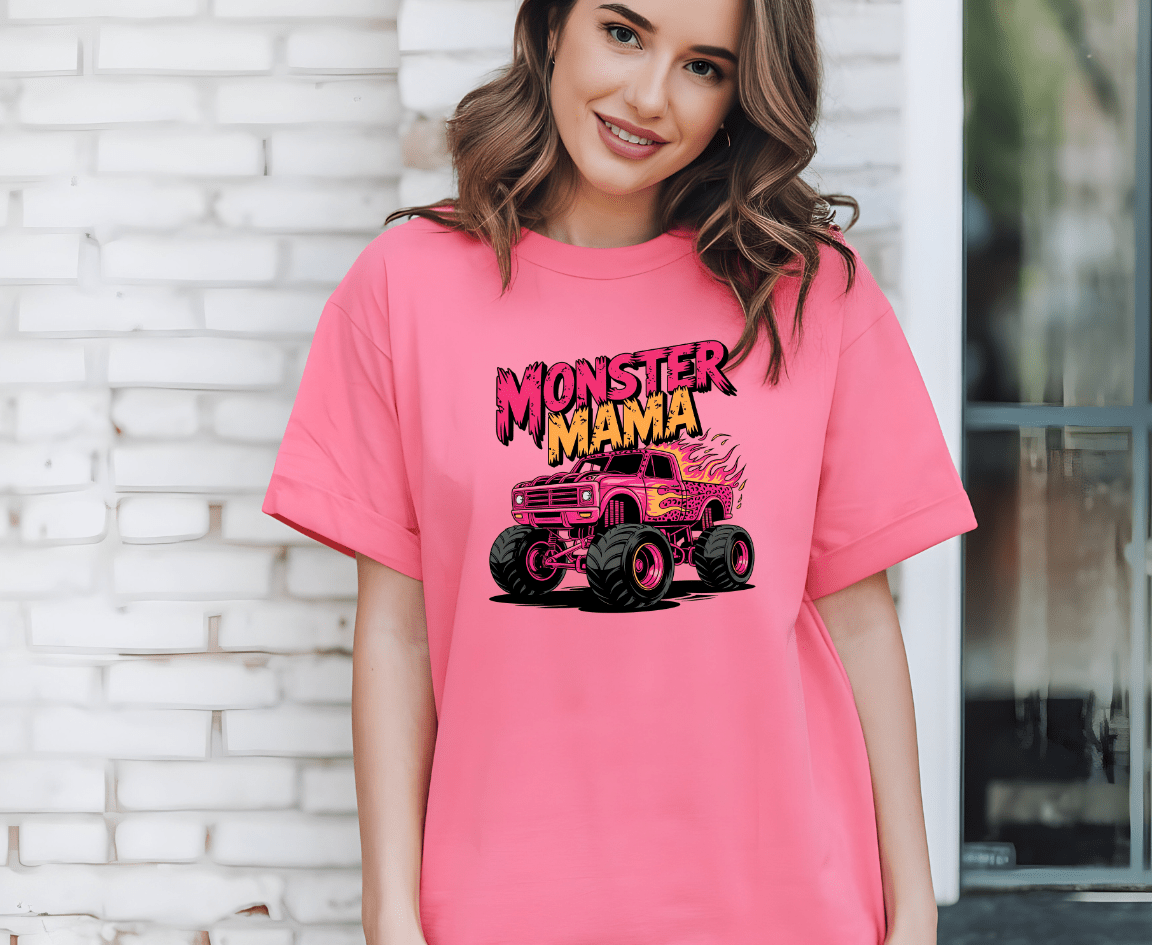 A smiling woman wears the Monster mama T-shirt by DB Custom Creations, featuring a cartoon monster truck and Monster Mama in bold graffiti-style text, printed with vibrant DTF printing. She stands before a white brick wall.