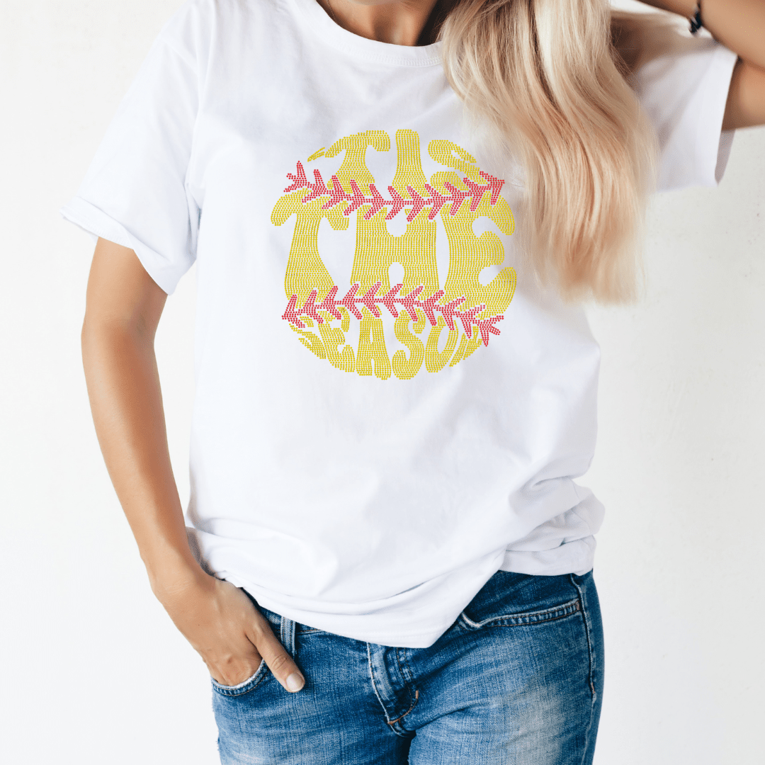 A person with long blonde hair and one hand in their pocket wears a white T-shirt featuring DB Custom Creations 10 x 10.5 Spangle Transfer - Softball Season design, paired with blue jeans.
