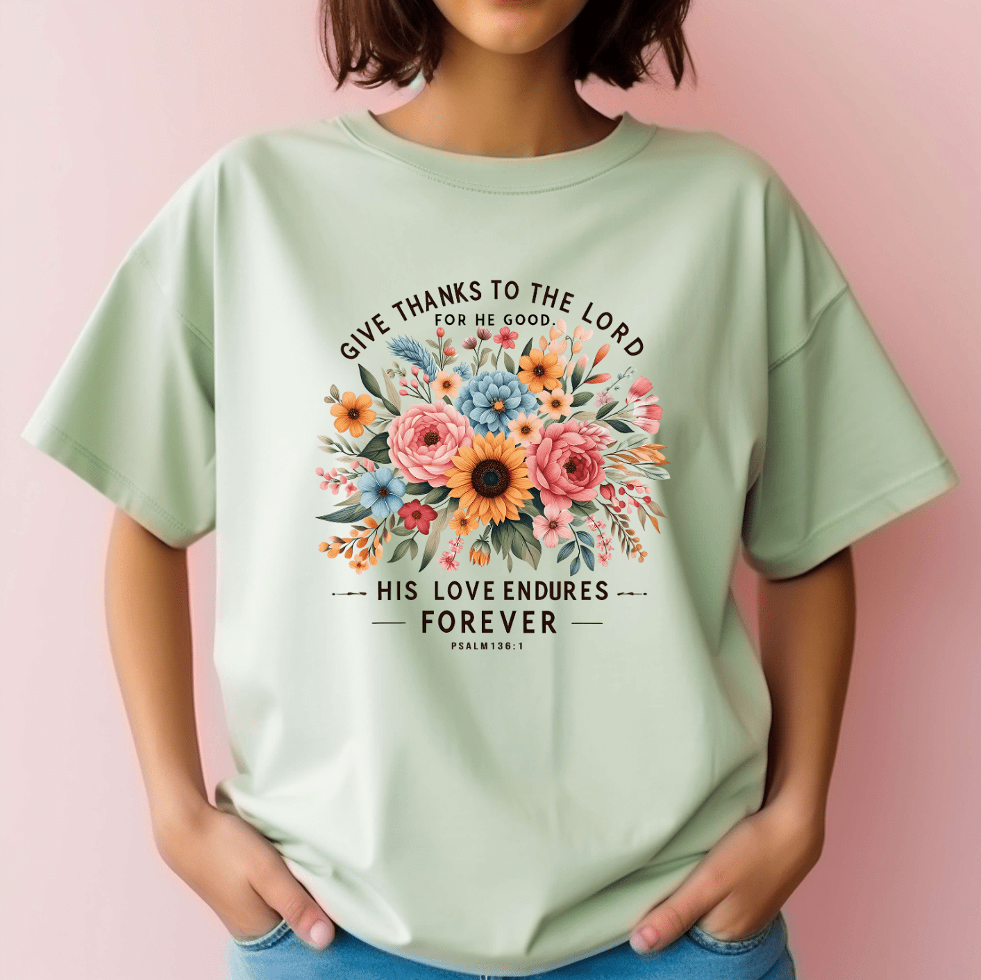 A woman wears DB Custom Creations Give thanks to the Lord light green t-shirt with a vibrant DTF-printed floral bouquet and the words, Give thanks to the Lord for He is good. His love endures forever. Psalm 136:1 on the front.