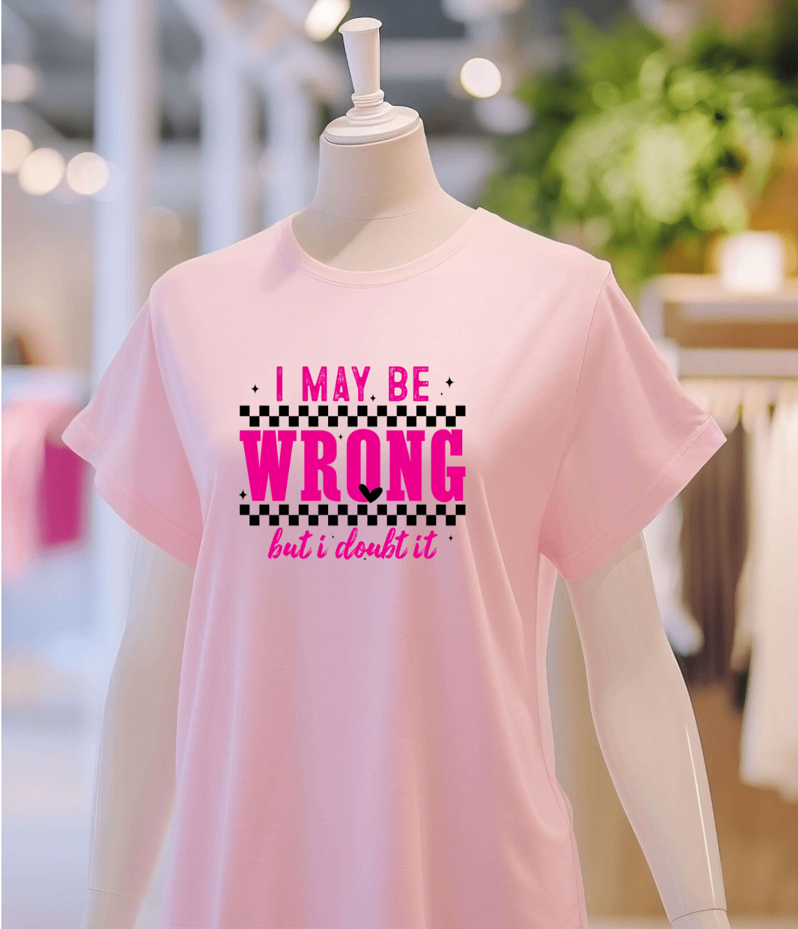 A mannequin models DB Custom Creations May be wrong light pink t-shirt, featuring bold pink and black text, in a brightly lit clothing store.