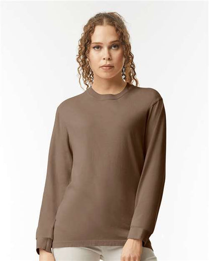A person with curly hair models the Comfort Colors 6014, a long-sleeved brown garment-dyed top made from ring spun cotton, standing against a plain white background and looking directly at the camera.