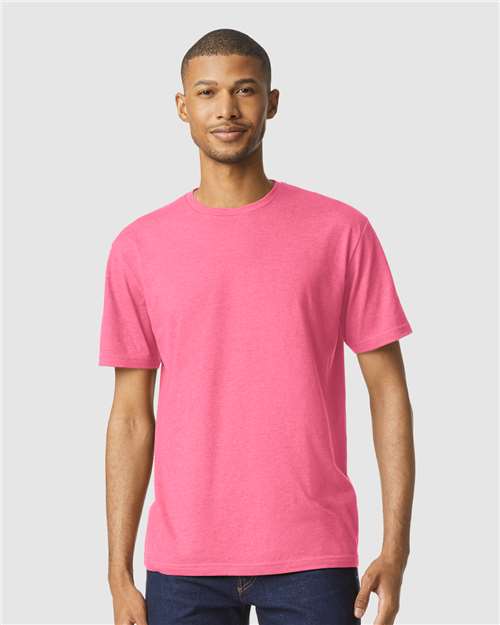 A man in a bright pink Gildan Softstyle 64000CVC t-shirt and dark jeans stands facing forward against a light gray background.