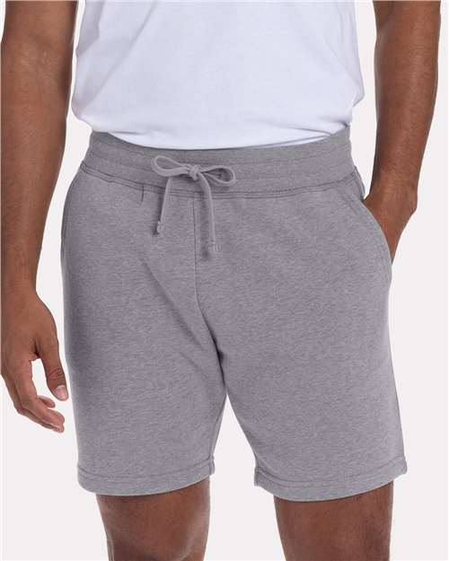 A person models the Next Level 9903: a white combed ringspun cotton t-shirt paired with light gray drawstring shorts, hands in pockets. The classic fit outfit is shown from waist to mid-thigh.