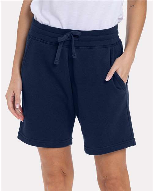 A person wearing Next Level 9903 classic fit white t-shirt and navy blue drawstring shorts, hands in pockets, shown mid-torso to mid-thigh against a plain background. Made from combed ringspun cotton for comfort and durability.