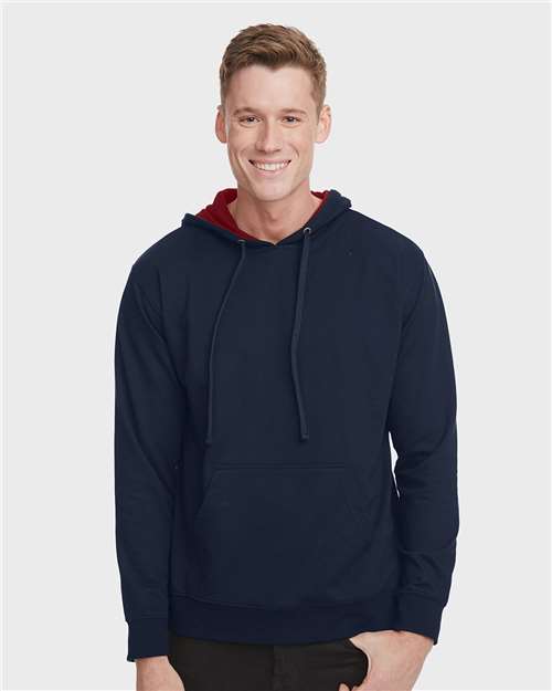 A smiling young man wears the Next Level 9301 navy blue french terry fleece hoodie with a red inner hood, standing against a plain light gray background.