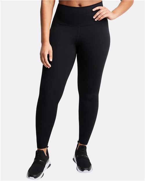 A person wearing Champion CHP120 high-waisted black recycled polyester leggings and black sneakers stands against a plain light background, one hand on their hip.
