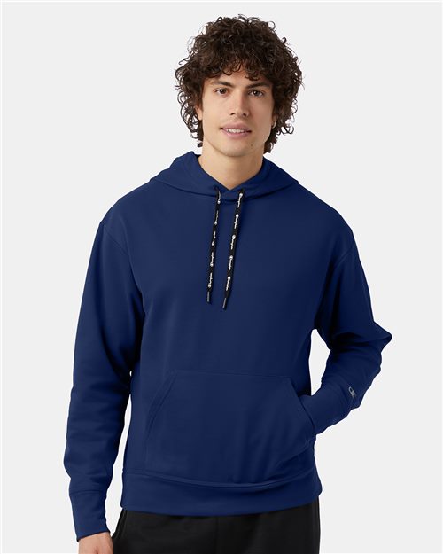 A young man with curly brown hair wears the Champion CHP180 navy blue recycled polyester fleece hoodie with a front pocket and black drawstrings, standing against a plain white background.