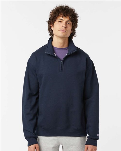 A young man with curly hair wears the Champion S450 navy quarter-zip fleece over a purple T-shirt and light gray pants, standing against a plain white background.