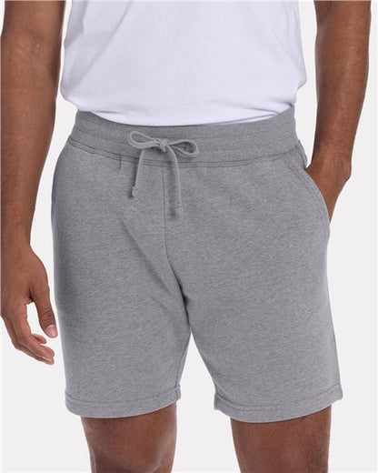 A model wears the Next Level 9903: a classic fit white combed ringspun cotton T-shirt and light gray drawstring shorts, hands in pockets, pictured waist to mid-thigh against a plain background.