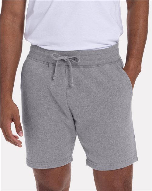 A model wears the Next Level 9903: a classic fit white combed ringspun cotton T-shirt and light gray drawstring shorts, hands in pockets, pictured waist to mid-thigh against a plain background.