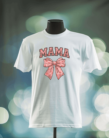 The Mama Bow t-shirt by DB Custom Creations is displayed on a mannequin, featuring bold, patterned pink MAMA lettering above a pink bow, printed with vibrant DTF Transfer, set against a softly blurred background with bokeh.