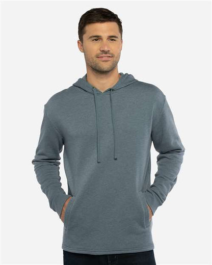 A man stands facing forward, wearing the Next Level 9300 blue-gray hoodie made from soft cotton-polyester fleece, hands in the front pockets, set against a light gray background.