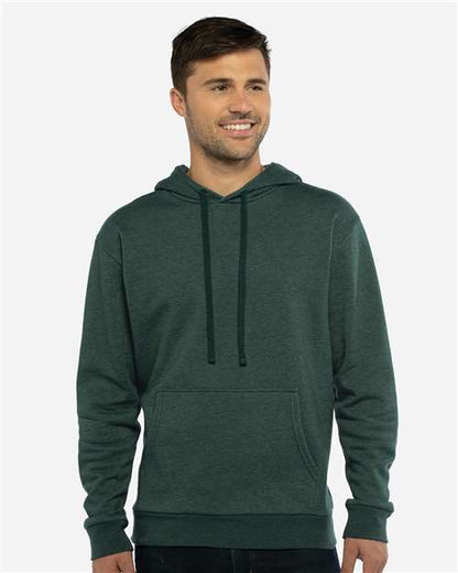A man smiles while wearing the Next Level 9302 dark green hoodie, crafted from soft cotton-polyester fleece with a front pocket and drawstrings, standing against a plain light gray background.