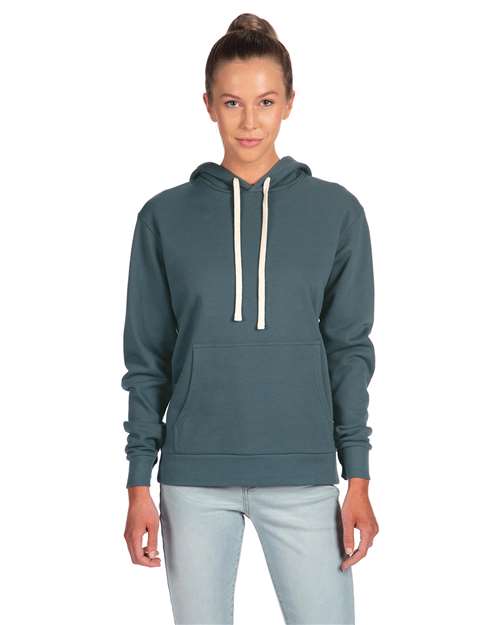 A woman with her hair in a bun and neutral expression faces forward, wearing the Next Level 9303 teal cotton-poly hoodie with jersey-lined hood, white drawstrings, and front pocket, paired with light blue jeans.