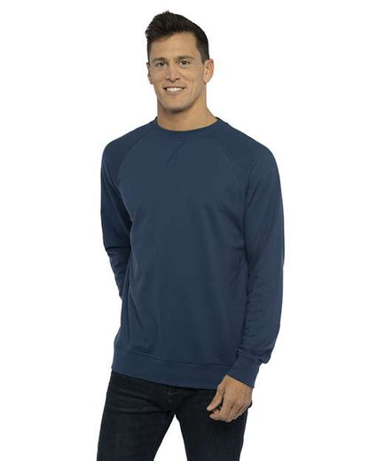 A man stands against a white background, smiling and wearing the Next Level 9000 navy blue long-sleeve crewneck sweatshirt made from cotton polyester fleece with dark jeans, one hand by his side and the other slightly in his pocket.