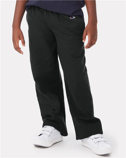 A child models Champion P890 black cotton-polyester sweatpants with side seam pockets and white sneakers, standing against a plain white background. Only the lower half of the body is shown.