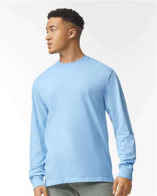 A young man in the Comfort Colors 6014 light blue garment-dyed, ring spun cotton long-sleeve shirt and green pants stands facing left, looking off to the side against a plain white background.
