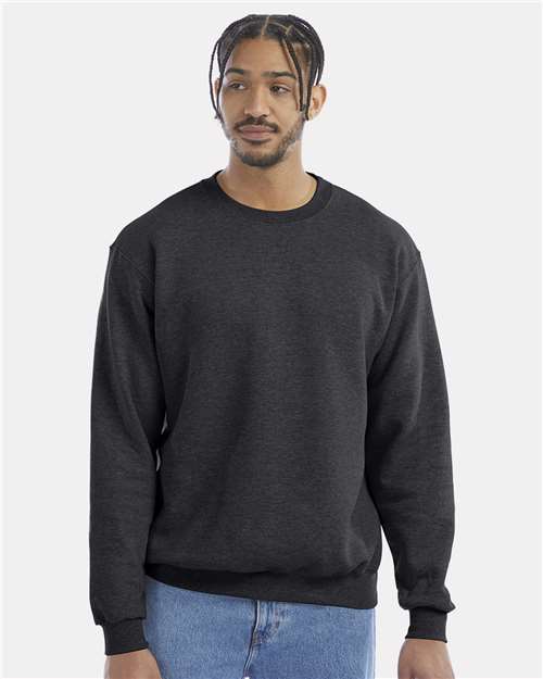 A man with braided hair wears the Champion S600 sweatshirt and blue jeans, standing against a light gray background. He looks slightly to the side with a neutral expression.