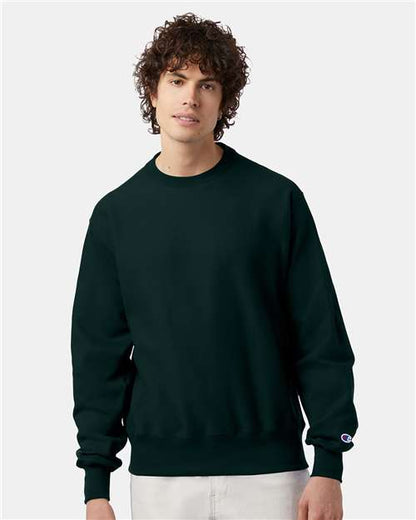 A young man with curly brown hair wears the Champion S149 sweatshirt and light pants, standing against a light gray background.