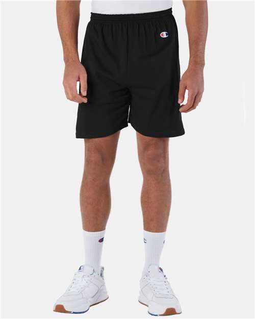 A person stands facing forward in Champion 8187 black athletic shorts, white crew socks with a logo, and white athletic sneakers. The upper body is not visible, and the background is plain white.
