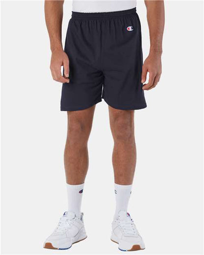 A person wears Champion 8187 shorts (100% cotton) and white crew socks, both featuring the Champion logo, with white sneakers. The upper body isnt shown; theyre standing against a light background.