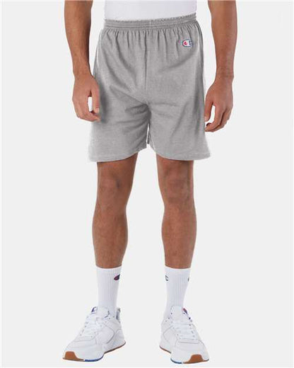 A person wears Champion 8187 light gray athletic shorts, white crew socks, and white sneakers, standing against a plain light background with only the lower half of the body visible.