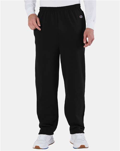 A person in black Champion P800 sweatpants featuring the logo on the left hip, a white long-sleeve shirt, and white sneakers stands against a plain light background. The sweatpants are made with recycled polyester.