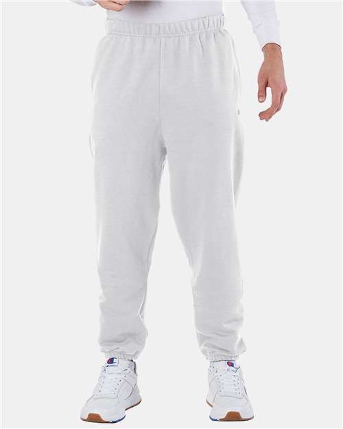 A person wears Champion RW10 light gray cotton-polyester sweatpants with elastic cuffs and white sneakers with blue and red details, standing against a plain white background. Only the lower half of the body is visible.