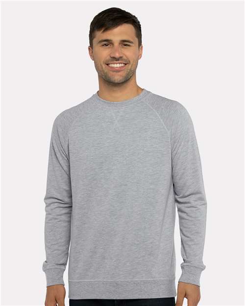 A man with short brown hair smiles, wearing a light gray Next Level 9000 crewneck sweatshirt made from cotton polyester fleece, standing against a plain light background.