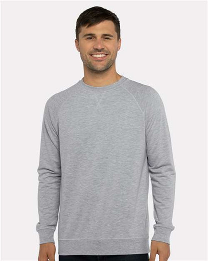 A man with short brown hair smiles, wearing a light gray Next Level 9000 crewneck sweatshirt made from cotton polyester fleece, standing against a plain light background.