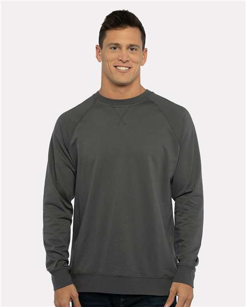 A man with short brown hair stands smiling in a Next Level 9000 dark gray fleece sweatshirt, featuring a classic v-notch neck, paired with dark jeans against a light gray background.