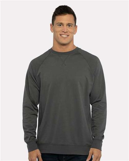 A man with short brown hair stands smiling in a Next Level 9000 dark gray fleece sweatshirt, featuring a classic v-notch neck, paired with dark jeans against a light gray background.