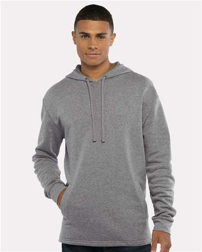 A young man stands facing forward, one hand in his pocket, smiling softly while wearing the Next Level 9300 light gray cotton-polyester fleece hoodie with drawstrings against a plain, light background.