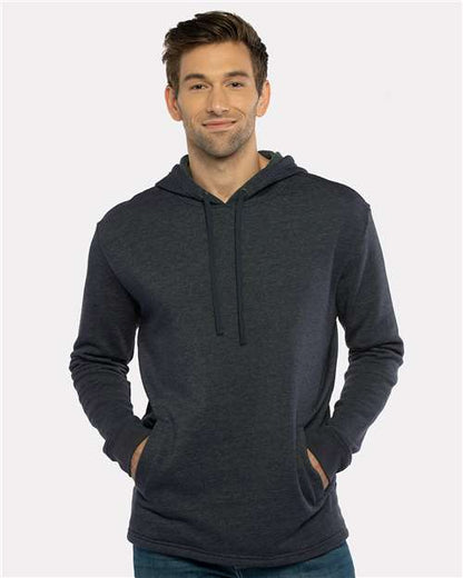 A man wears the Next Level 9300 hoodie, made from cotton polyester fleece, standing against a light background with hands in the front pocket, facing the camera and smiling softly.