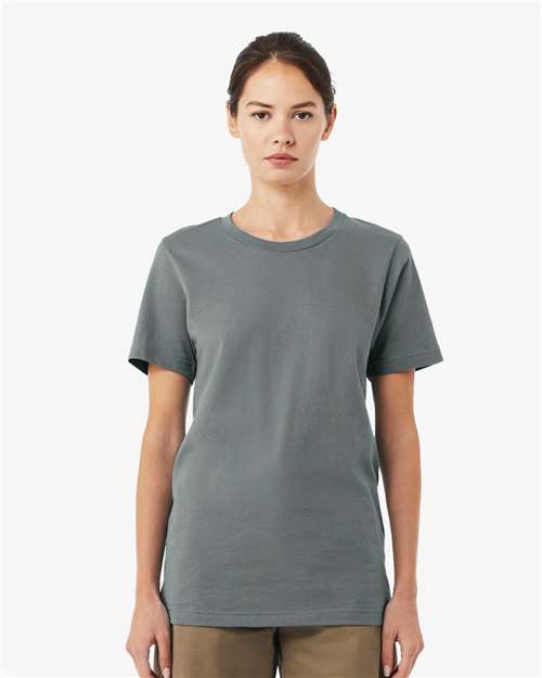 A woman with brown hair tied back stands facing forward, wearing a BELLA + CANVAS 3001 plain gray unisex t-shirt made from Airlume combed and ring-spun cotton and brown pants, set against a light gray background.