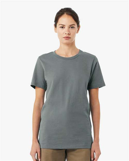 A woman with brown hair tied back stands facing forward, wearing a BELLA + CANVAS 3001 plain gray unisex t-shirt made from Airlume combed and ring-spun cotton and brown pants, set against a light gray background.