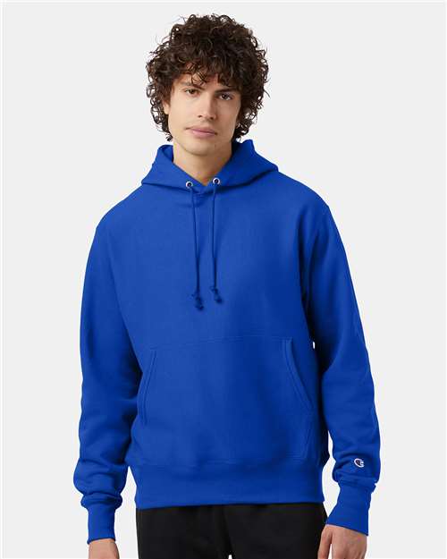 A young person with curly hair wears the Champion S101 sweatshirt, bright blue with a front pocket and drawstrings, standing against a plain light background.