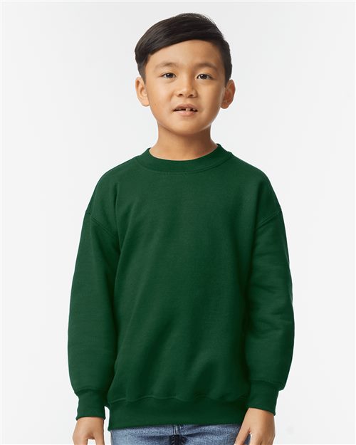 Young boy with short black hair wearing a Gildan 18000B Heavy Blend crewneck sweatshirt in dark green and blue jeans, standing against a plain white background.