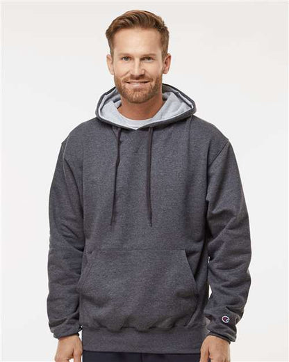 A man with short light brown hair and a beard is wearing the Champion S171 dark gray hoodie, featuring an embroidered logo and pouch pocket, standing against a plain light background and smiling slightly at the camera.