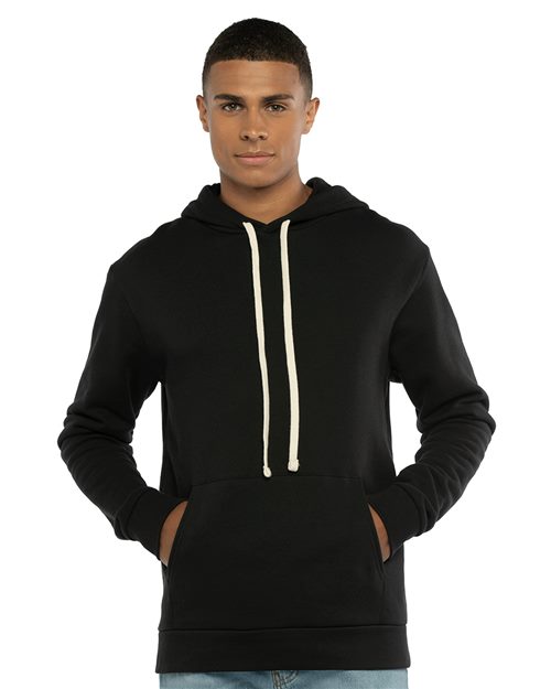 A young man stands facing forward against a white background, hands in the pocket of a Next Level 9303 black cotton-polyester hoodie featuring a jersey-lined hood and white drawstrings.