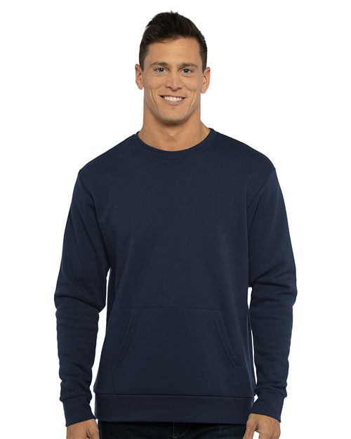 A man with short dark hair smiles, wearing the Next Level 9001 unisex navy blue crewneck sweatshirt made from cotton/polyester fleece with a front pocket, standing against a white background.